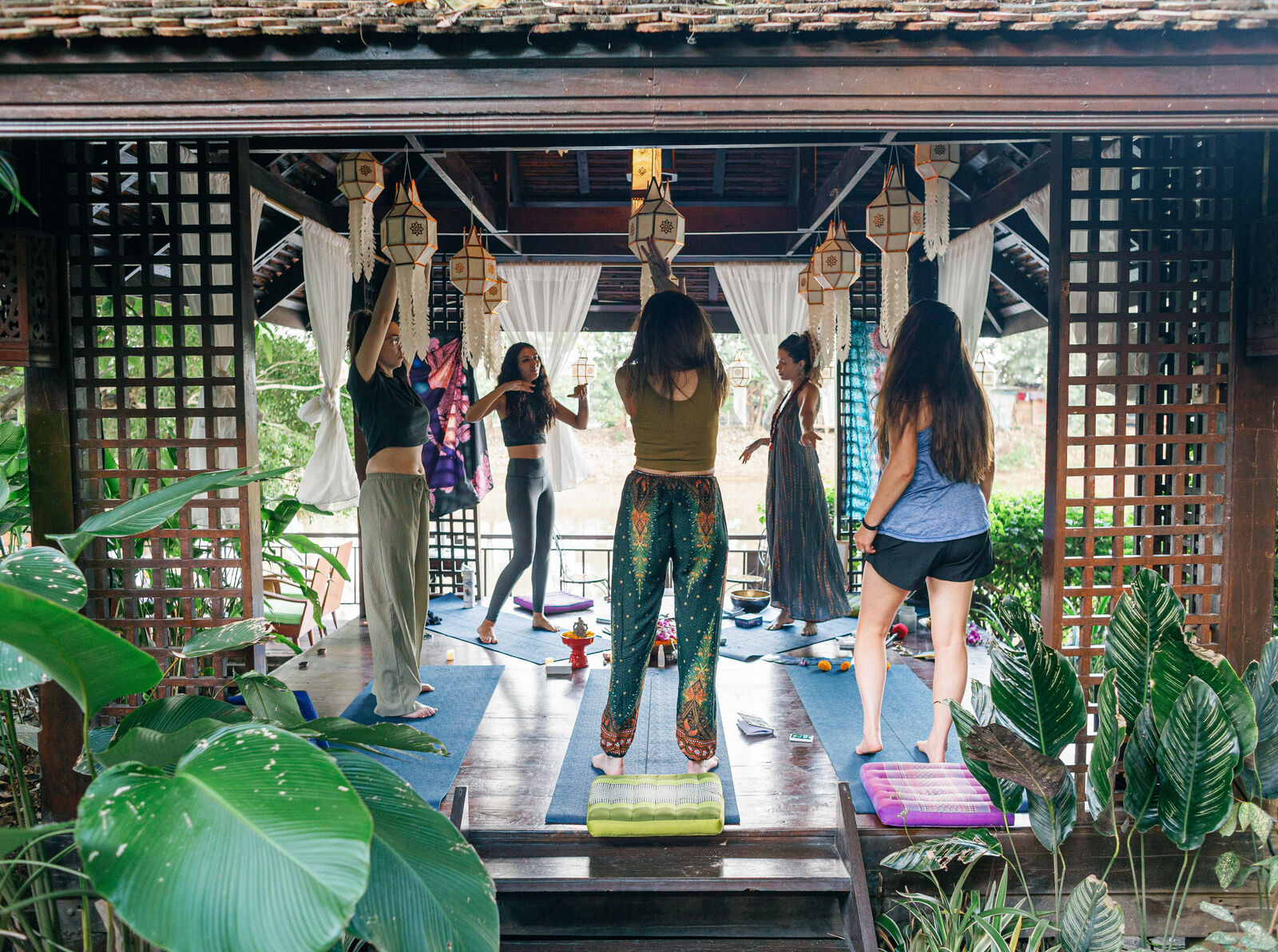 Women moving together on the open pavilion at the retreat villa, lanterns overhead, tropical garden beyond.