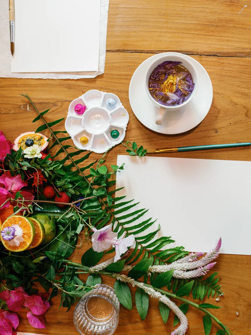Watercolour supplies, tropical flowers, and butterfly-pea tea on a wooden table at the retreat.